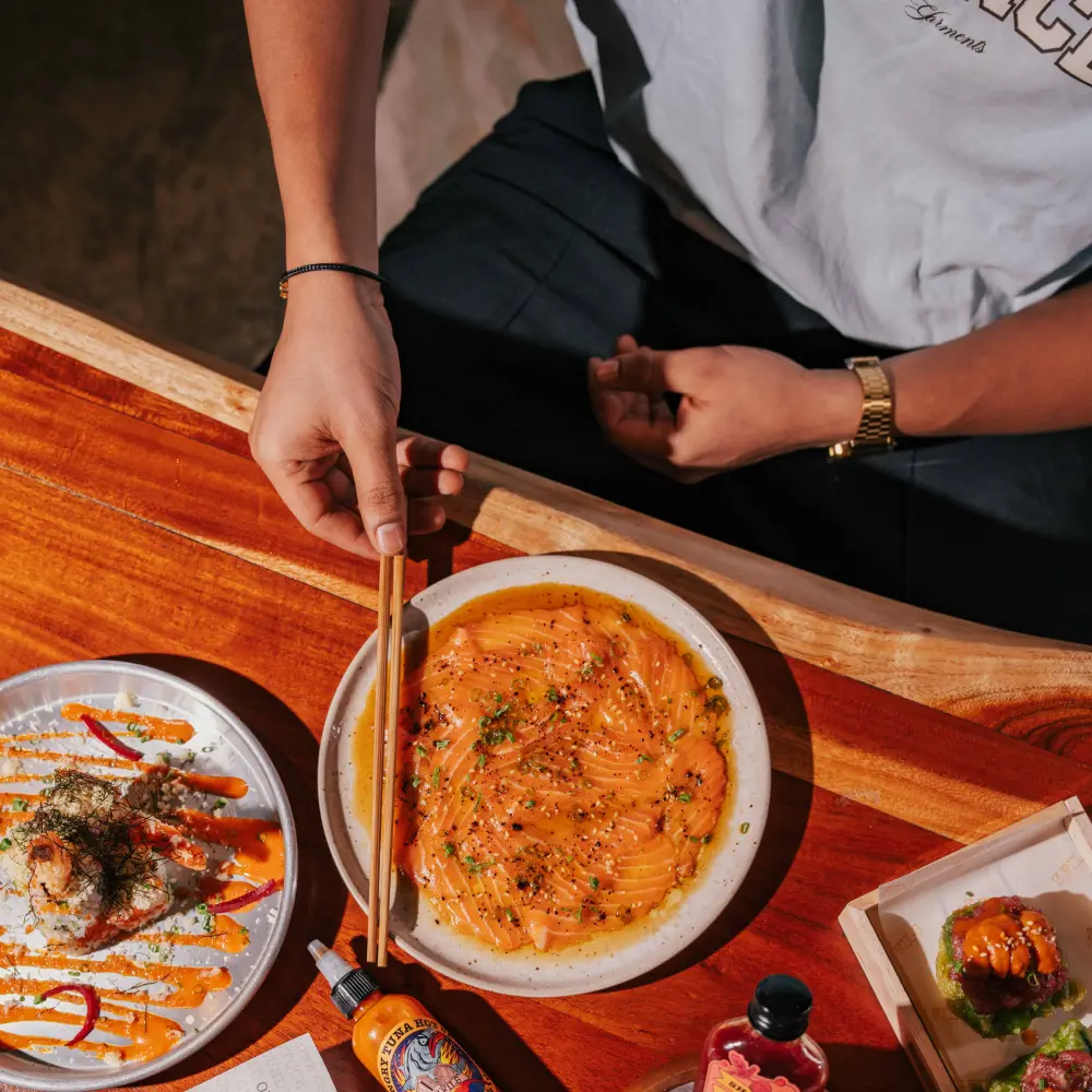 Hands with chopsticks over shared plates of salmon sashimi